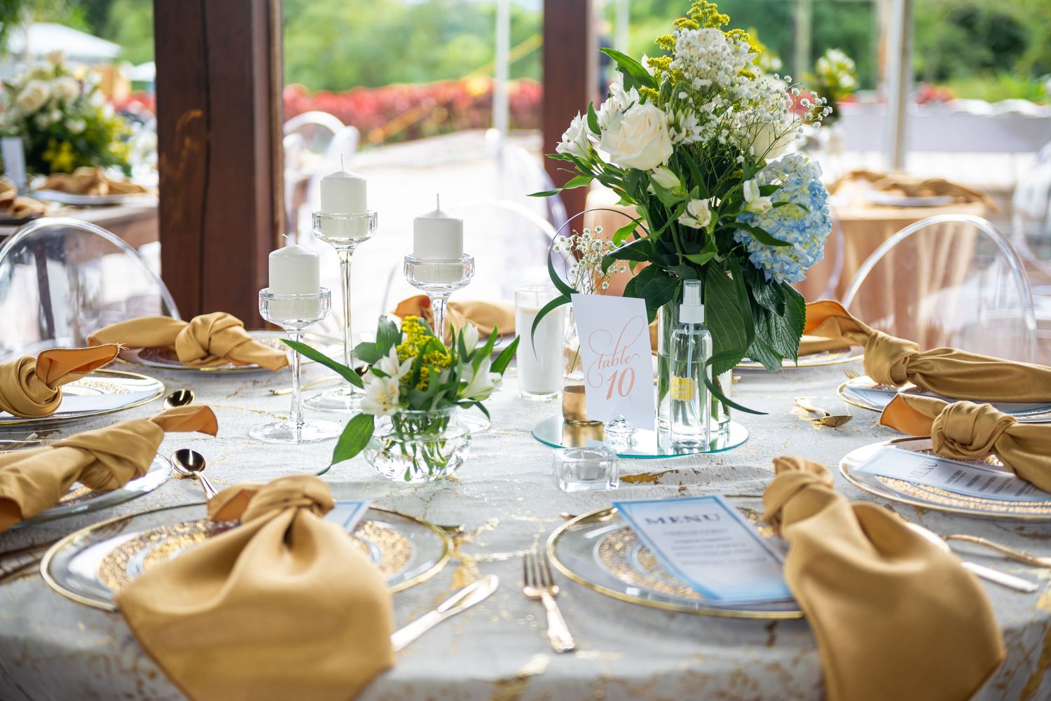 Round wedding reception table with white floral centerpieces, gold napkins, and formal place settings.