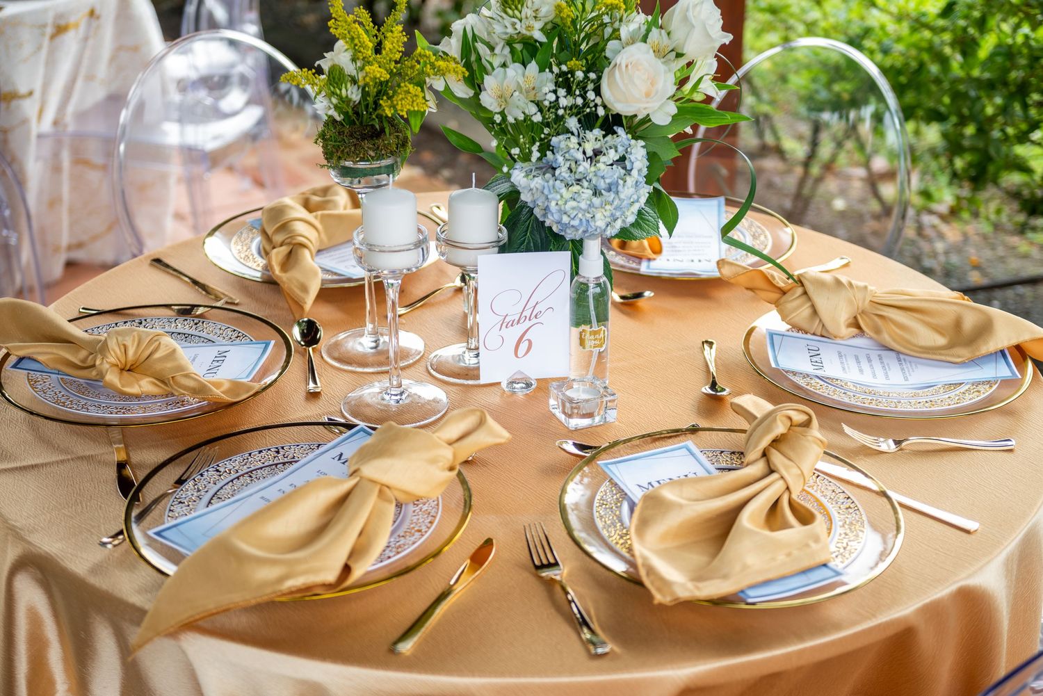 Formal round dining table with gold napkins, crystal plates and fresh flower centerpiece for wedding reception.