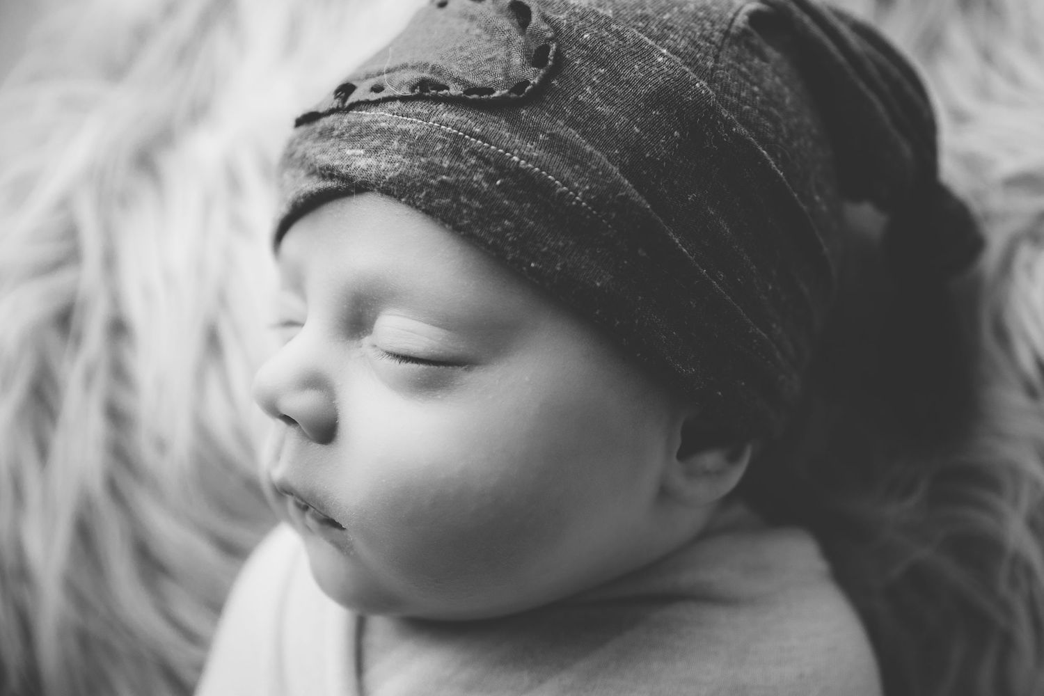 Sleeping infant wearing gray knit cap in monochrome close-up portrait.