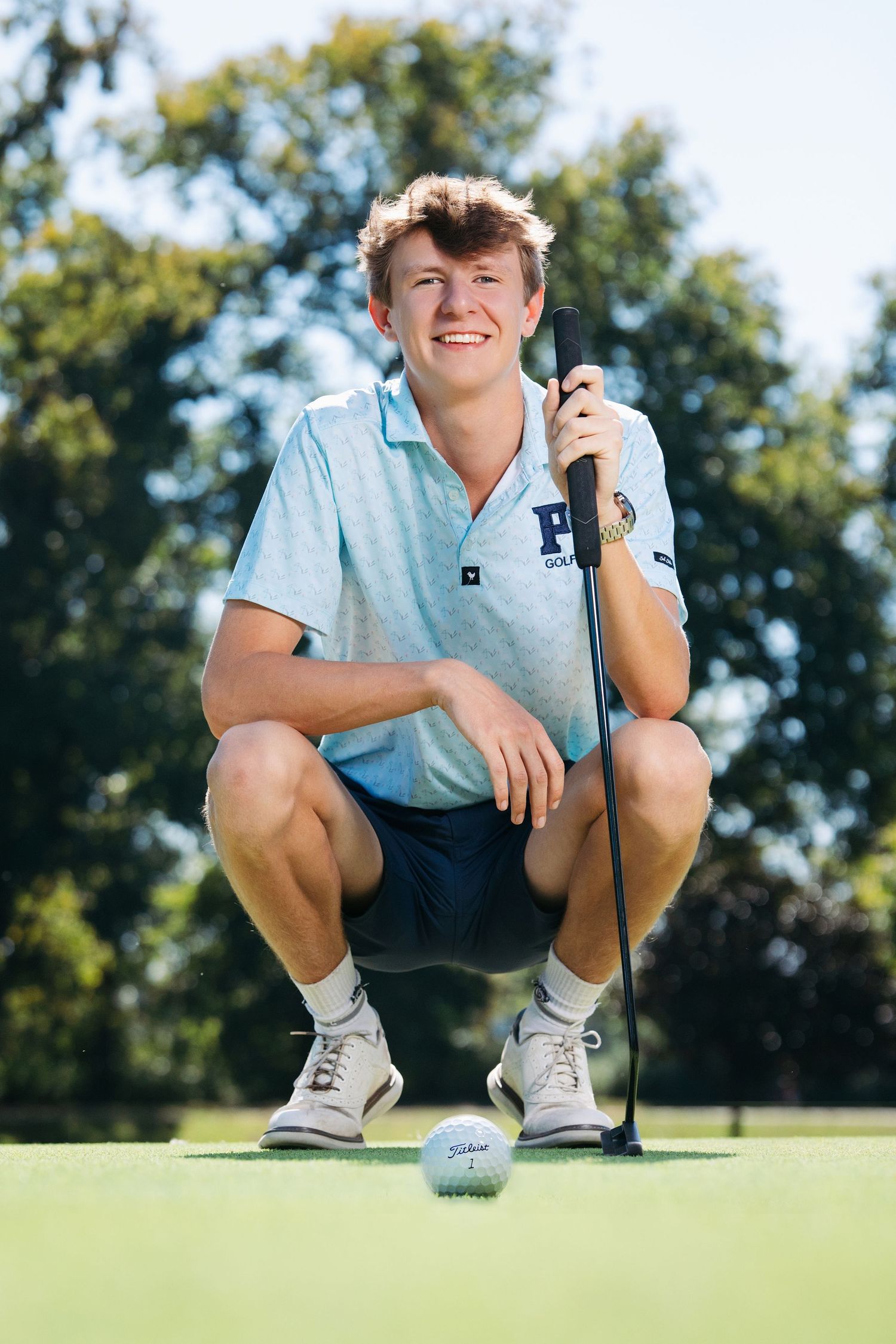 Nashville senior guy golfer in light blue polo analyzing putting green during sunny day. Middle TN senior photographer.