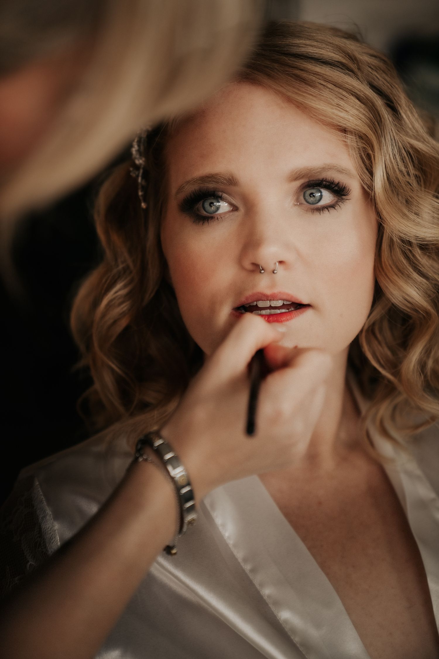 Close-up shot of makeup application with red lipstick on person with curled blonde hair.