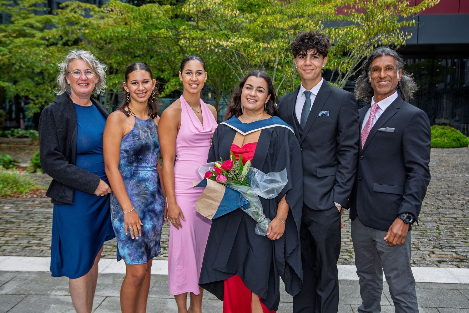 Graduation celebration group photo with family members in formal attire on campus grounds.
