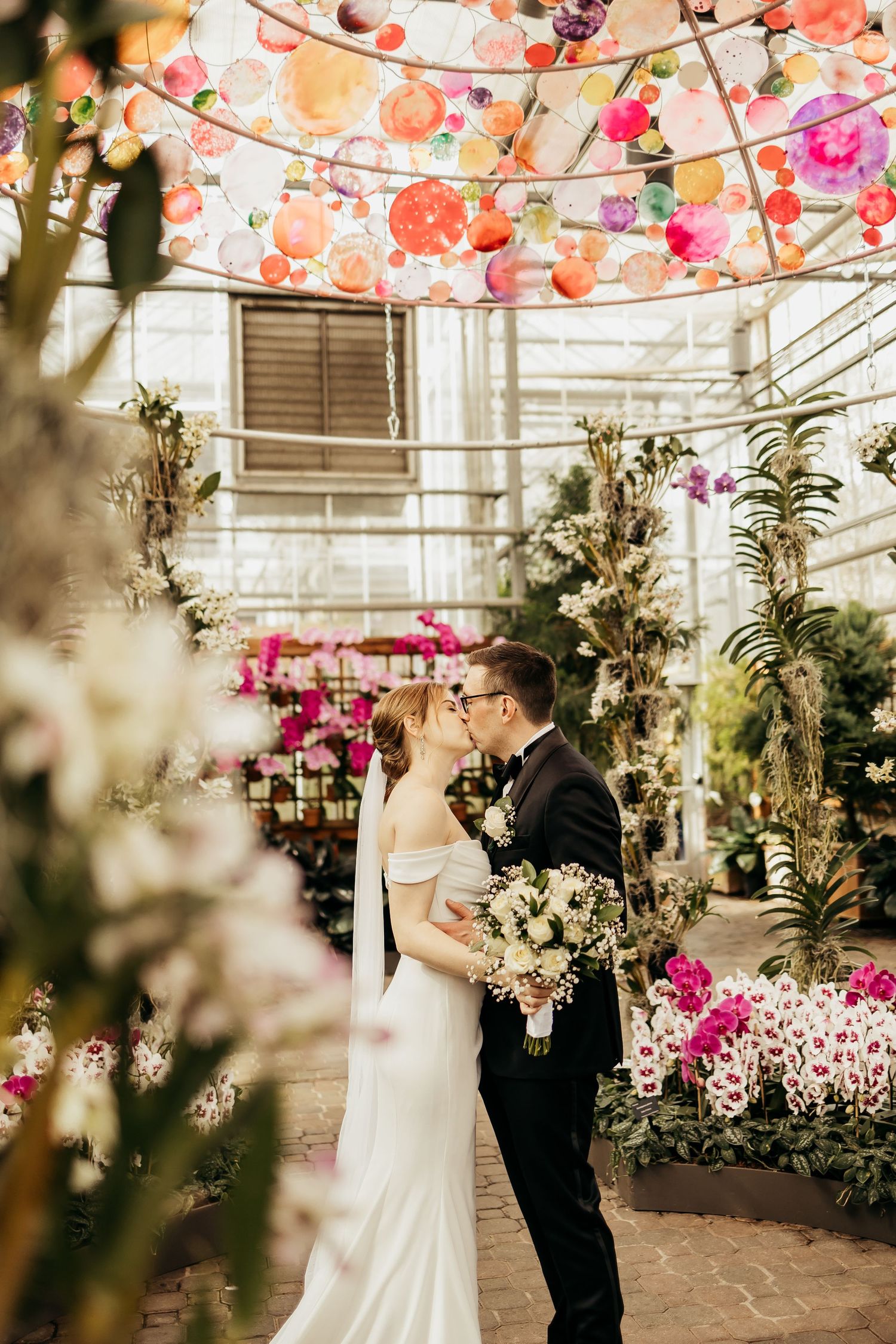 A couple dances beneath pink lanterns in a greenhouse filled with orchids.