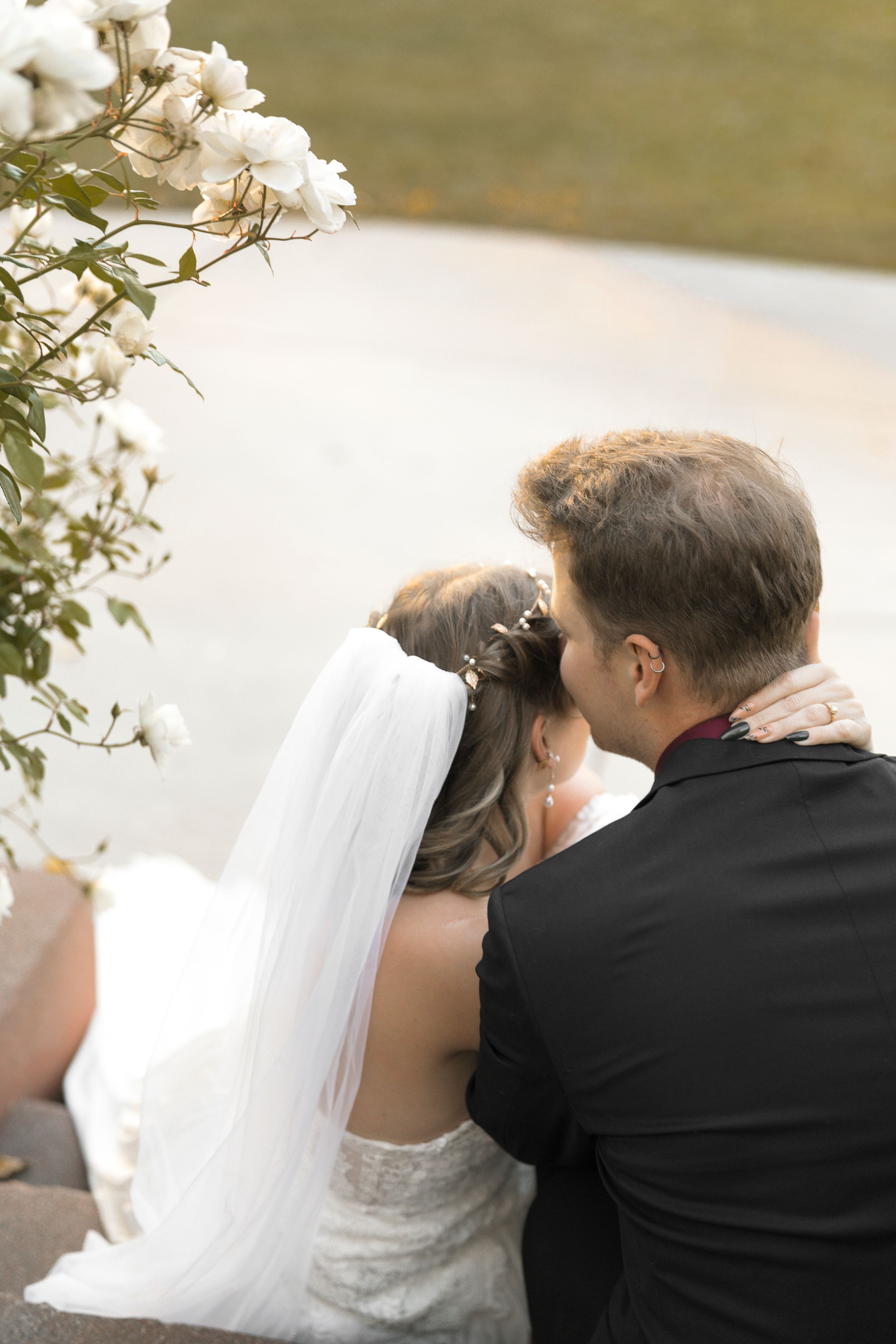 A couple shares an intimate moment during their wedding ceremony as they sit together outdoors in formal attire.