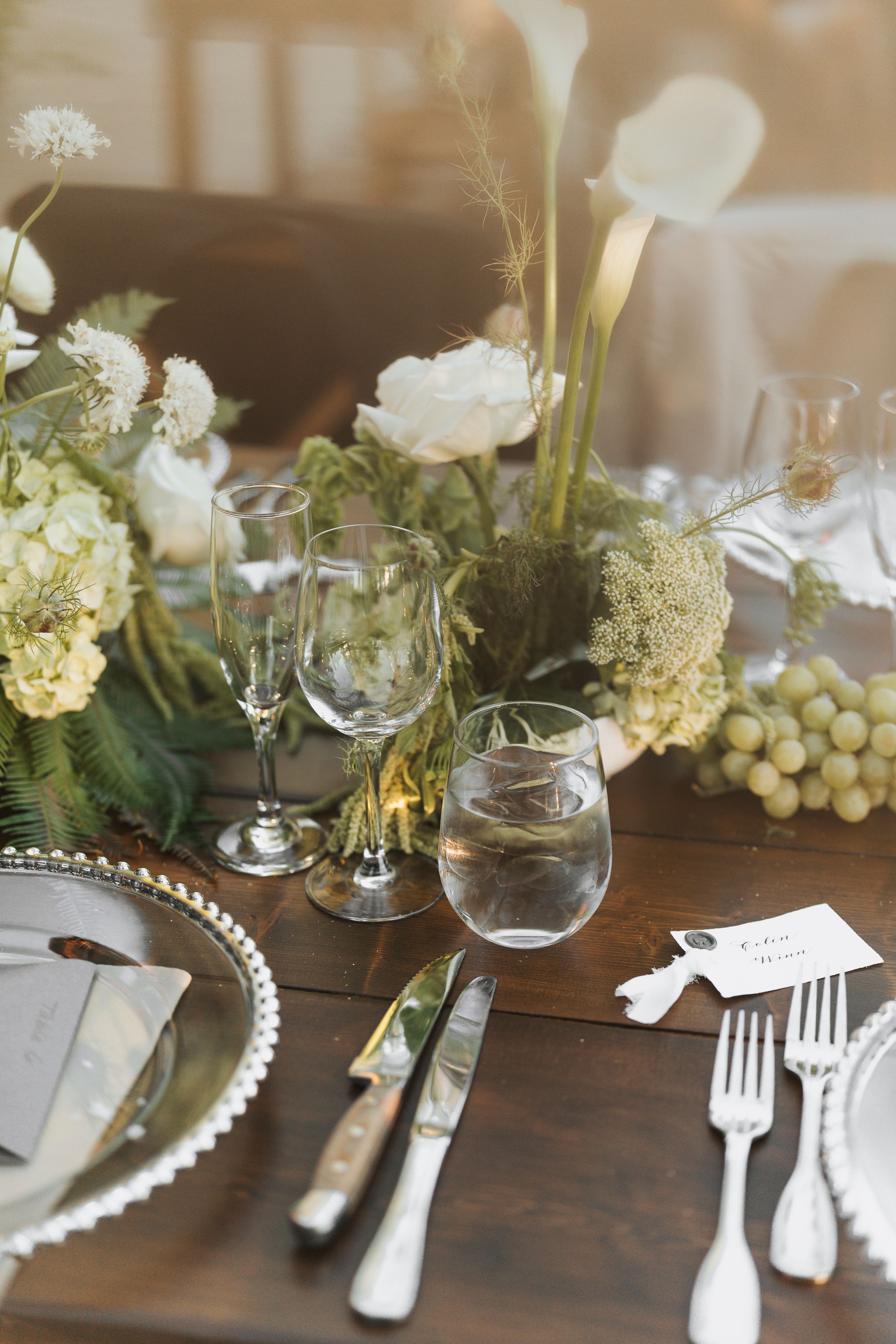 Elegant table setting with white flowers, grapes, and pearl-edged plates on a dark wooden surface.