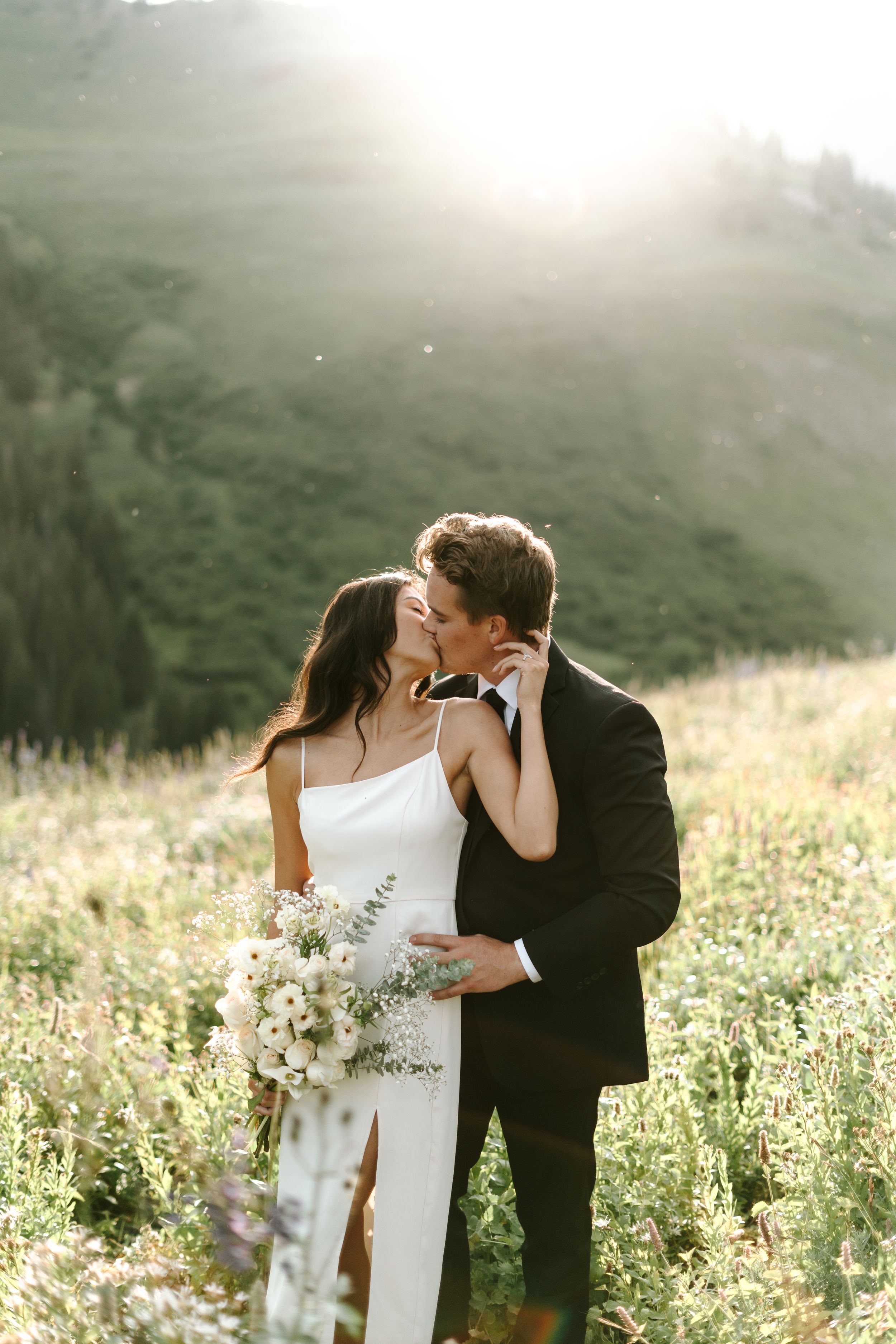 Romantic wedding couple embracing in a sunlit meadow at golden hour.
