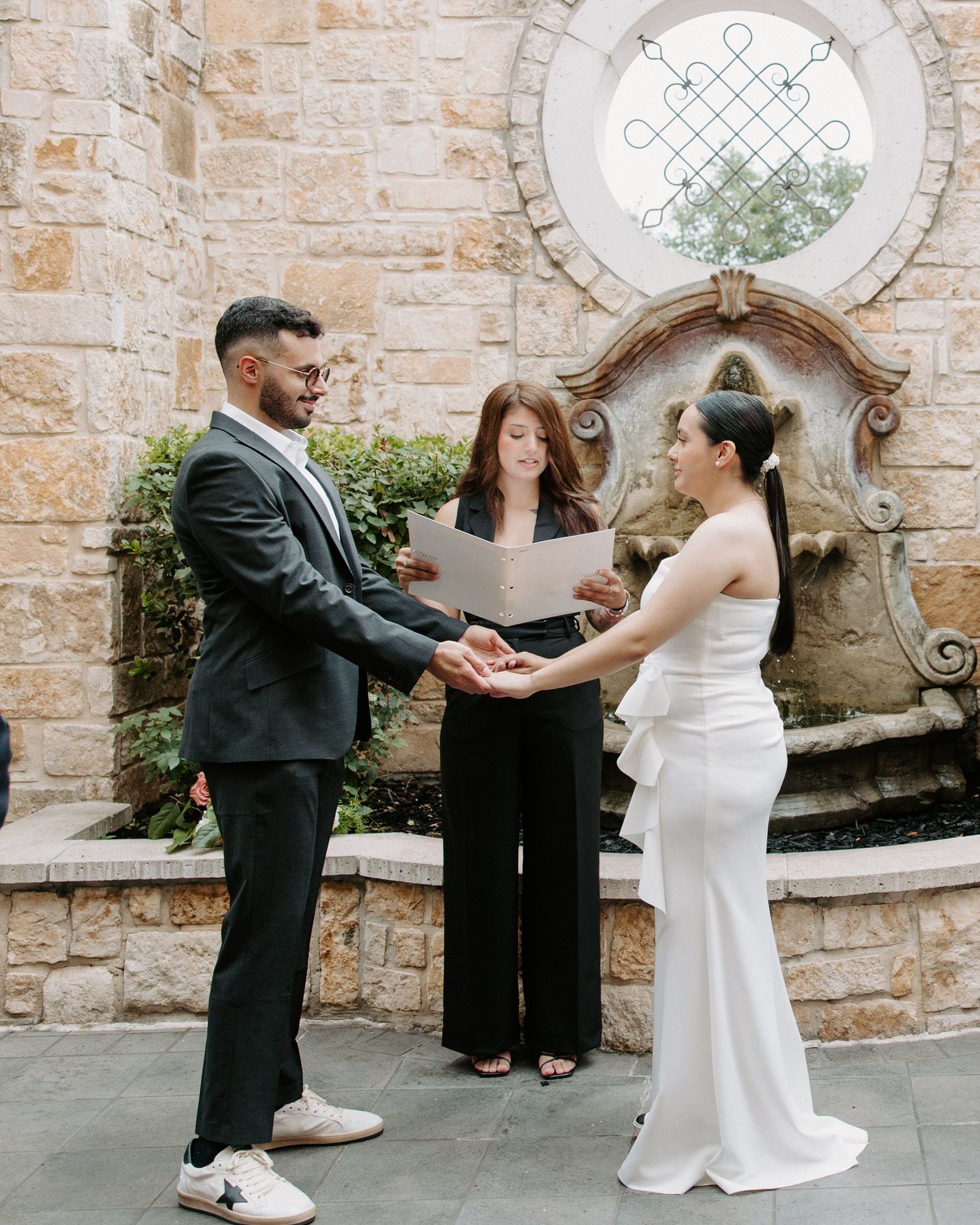 San Antonio Wedding Photography. Wedding ceremony taking place in front of stone archway with ornate circular window.
