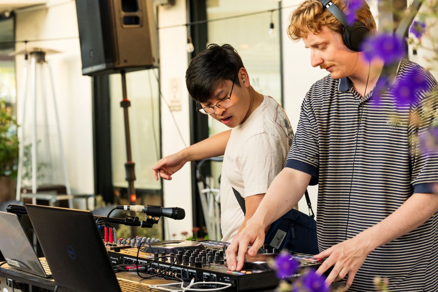 DJs collaborating on electronic music equipment at an outdoor venue.