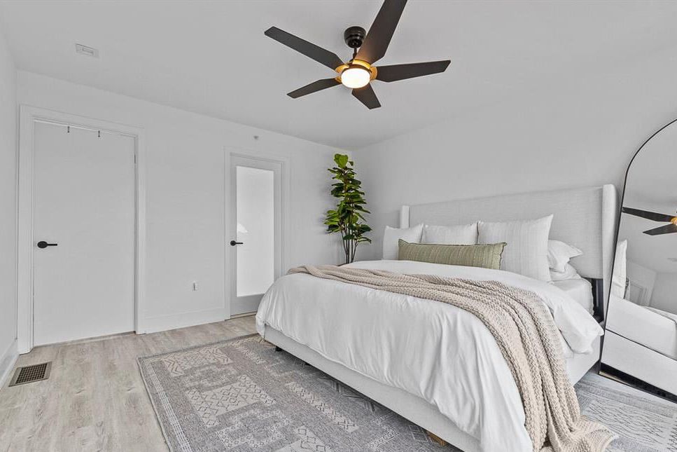 Modern bedroom with ceiling fan, light wood floors, white bedding, and minimalist decor.