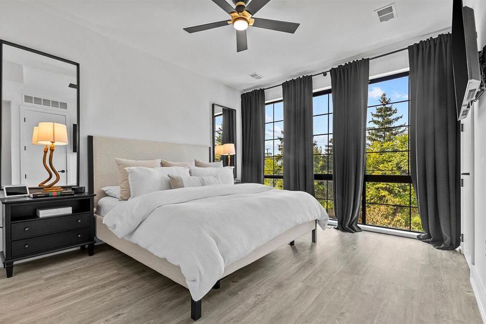 Bright master bedroom with floor-to-ceiling windows, ceiling fan, and dark wood furniture.