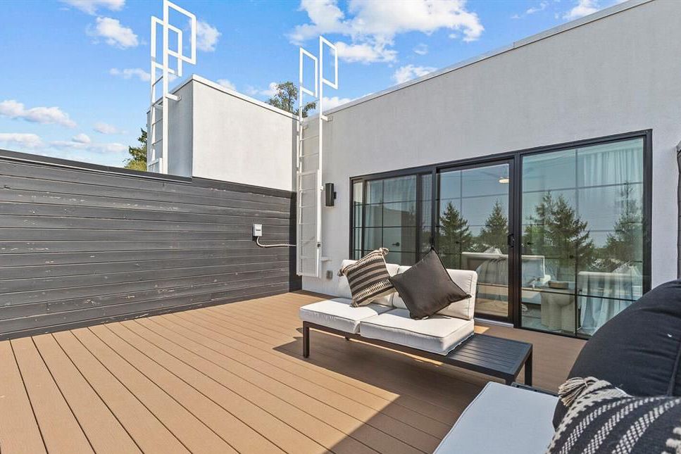 Modern rooftop terrace with composite decking, outdoor seating, and privacy wall under blue sky.