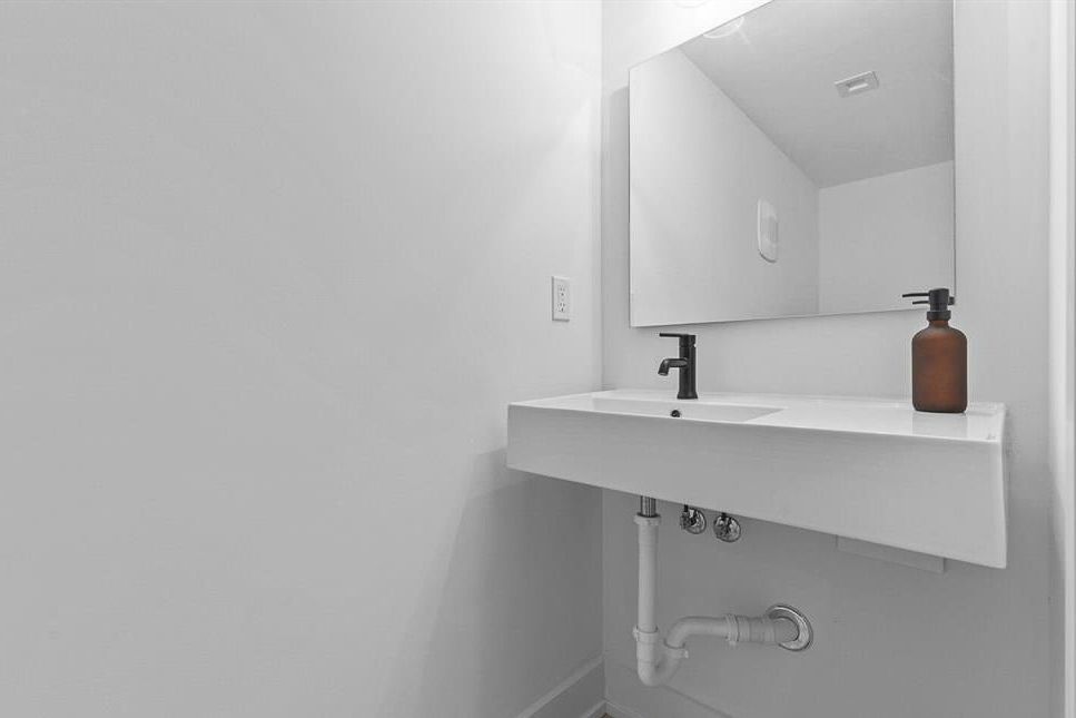 Minimalist white powder room with floating sink, black faucet, and large mirror.