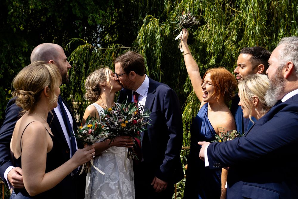 Wedding party celebrating outdoors under weeping willow trees.