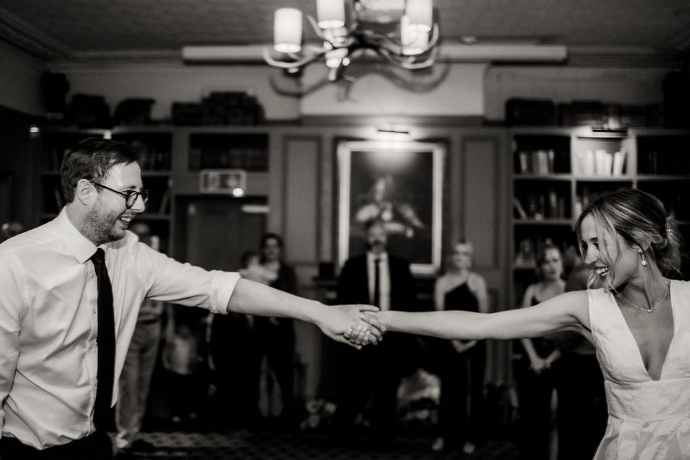 A couple dances together at an indoor reception venue with moody lighting and a chandelier above.