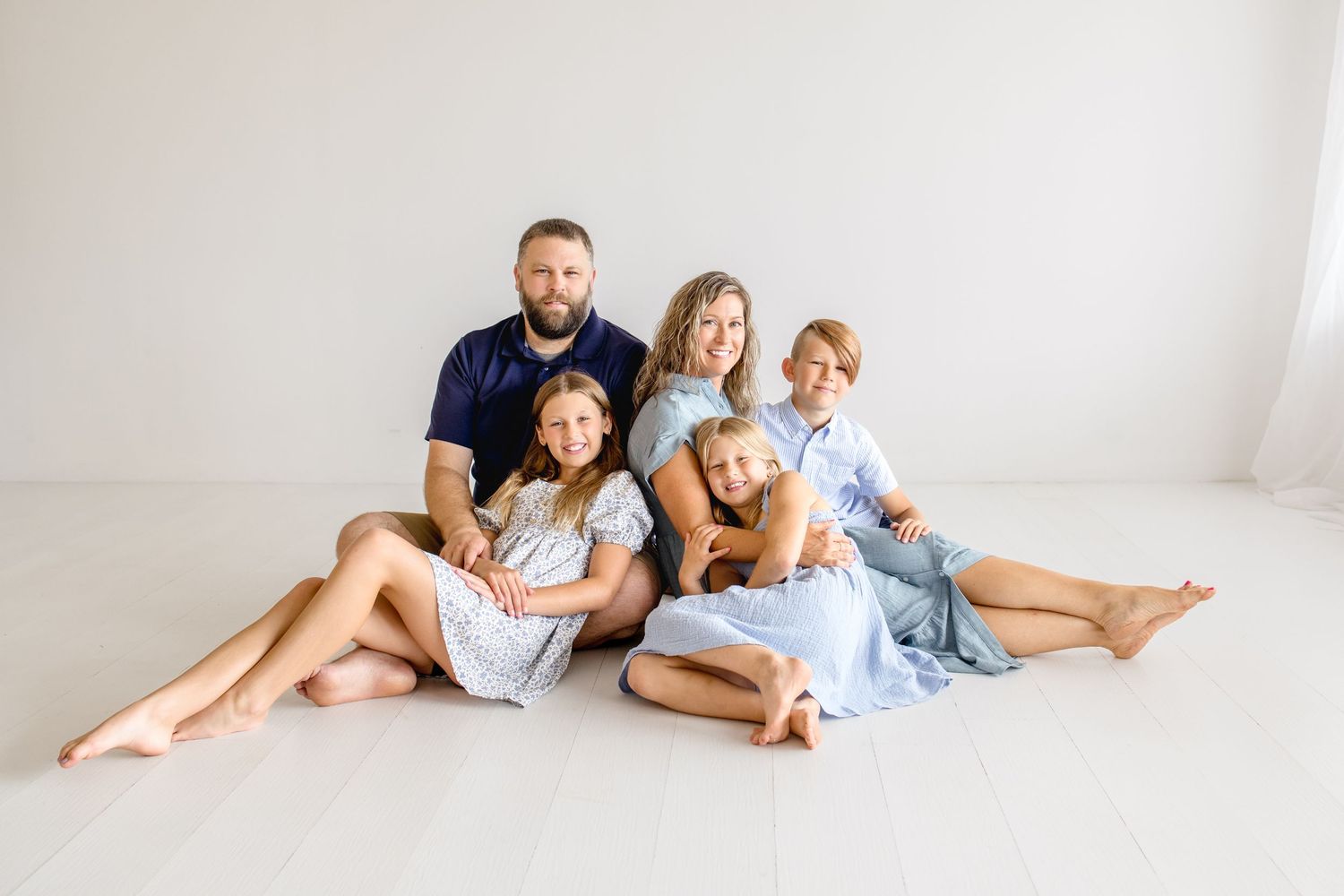 A family group sits together on the floor in coordinated blue and white outfits against a white backdrop.