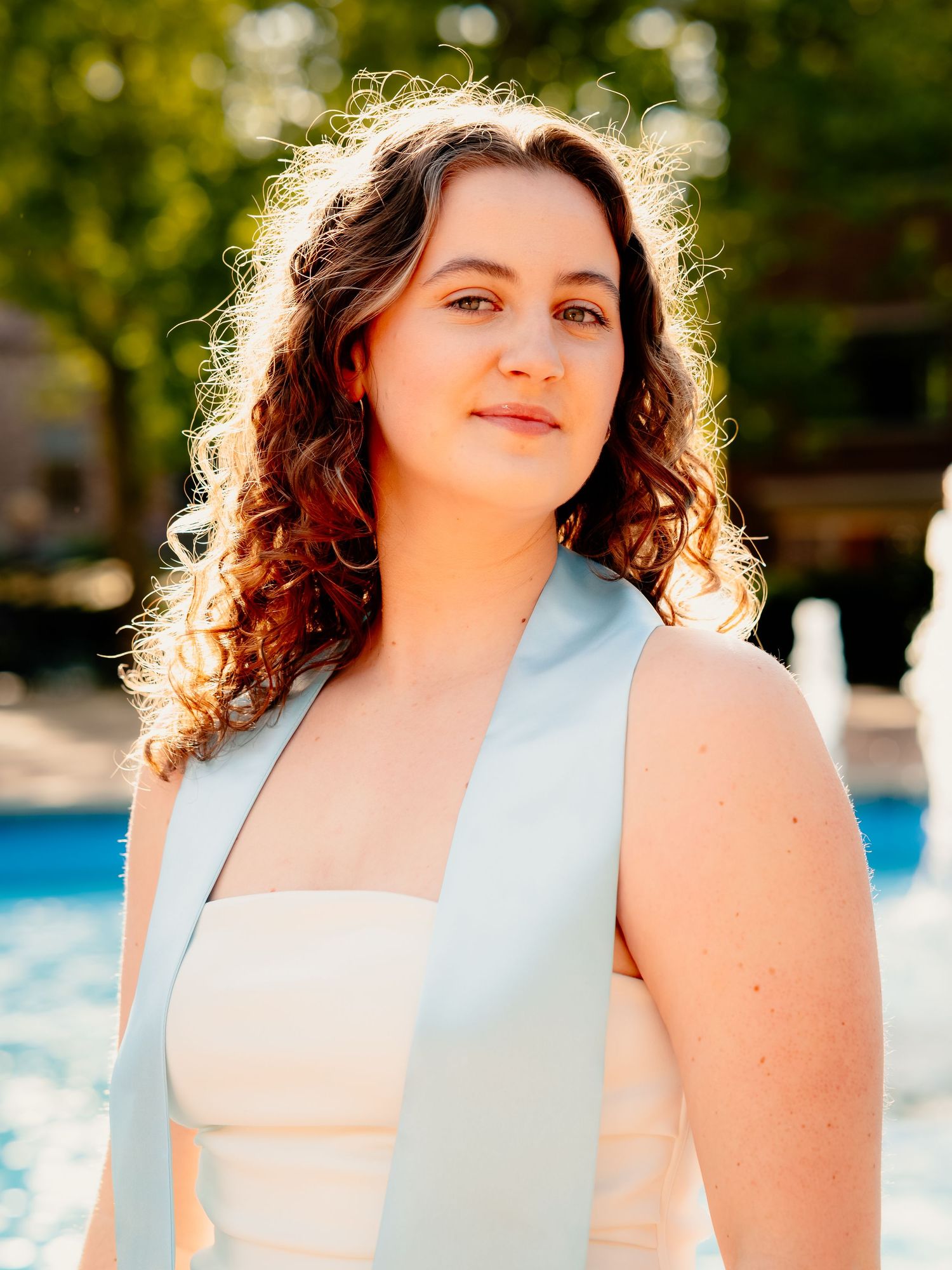 Backlit outdoor portrait session by a pool featuring a light blue outfit.