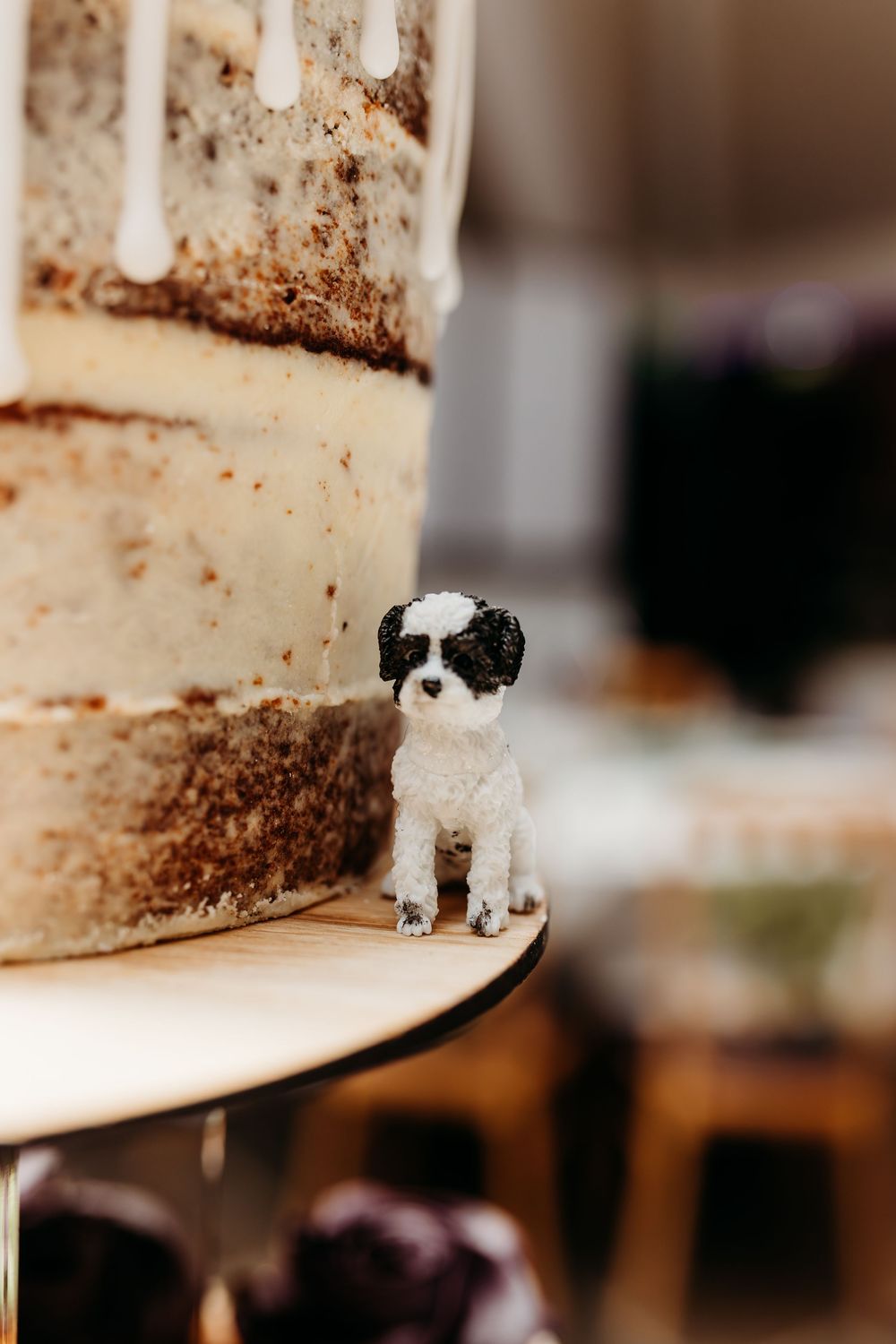 A small black and white dog toy stands at the edge of a wooden surface by wedding bake with a blurred background.
