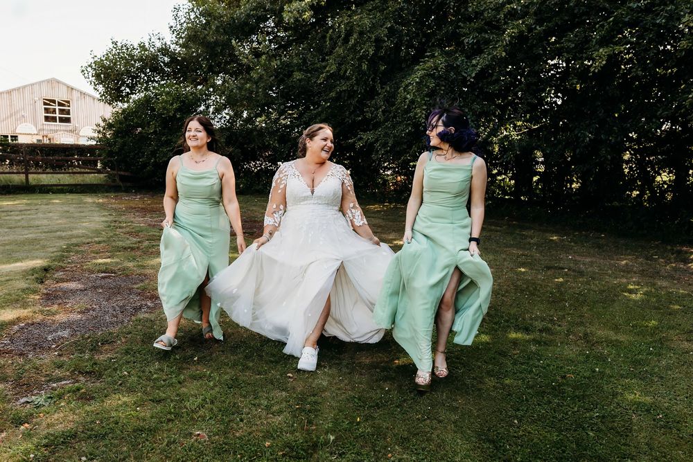 A wedding party in mint green bridesmaid dresses and white gown runs playfully across a grassy lawn on a sunny day.
