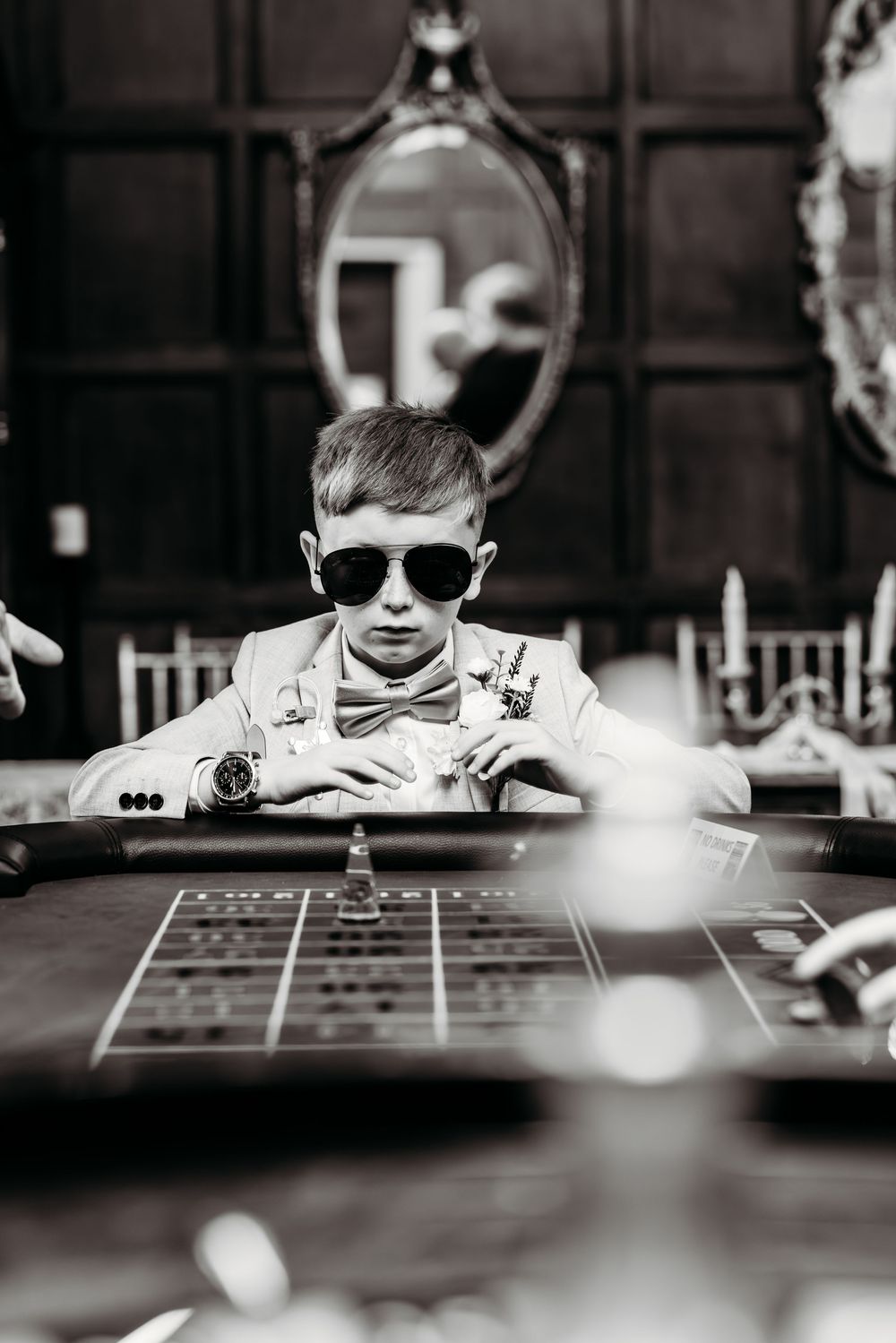 A young boy in sunglasses peers over a table in a dramatic black and white composition.