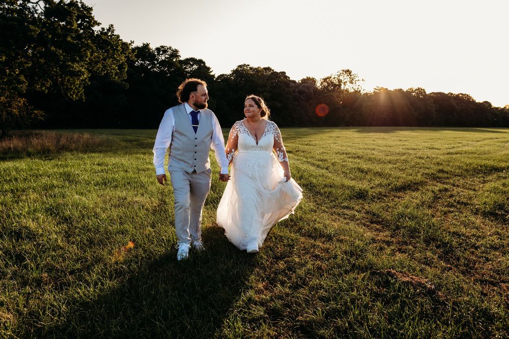 A couple walks together across a grassy field at sunset during their outdoor wedding celebration.