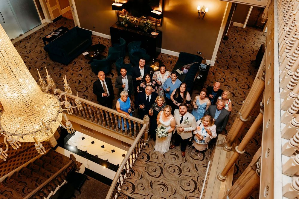 Overhead view of wedding guests gathered on grand staircase with ornate chandelier.