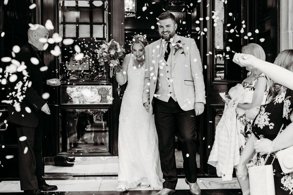 Black and white wedding ceremony photo with confetti falling at venue entrance.