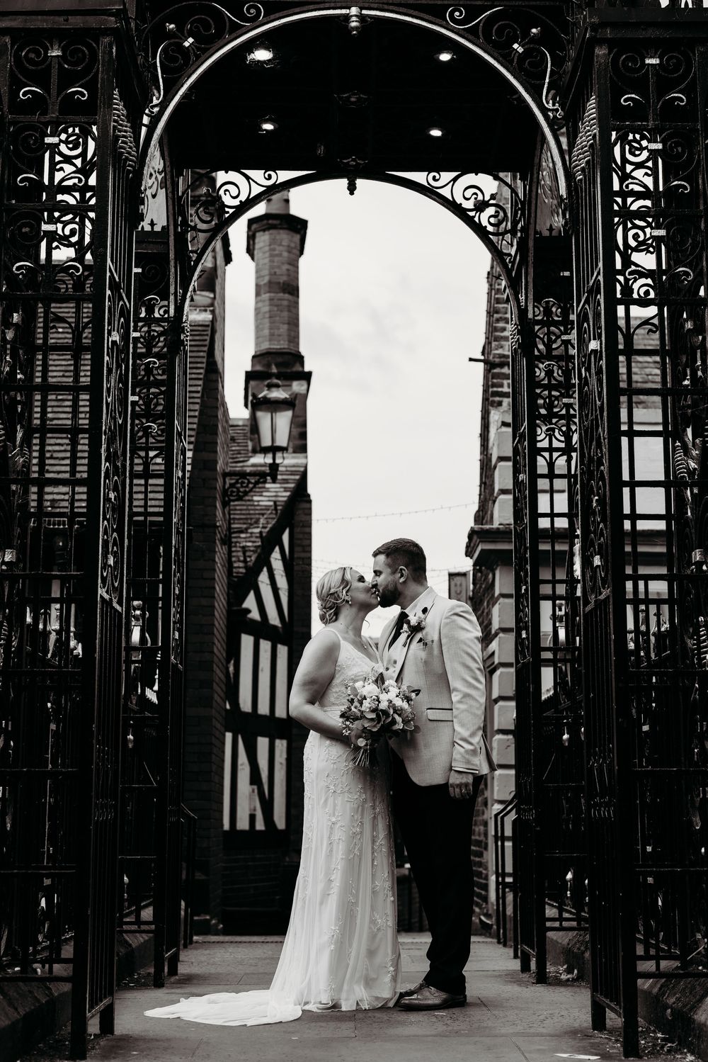 Dramatic black and white photo through ornate iron gates showing romantic moment.