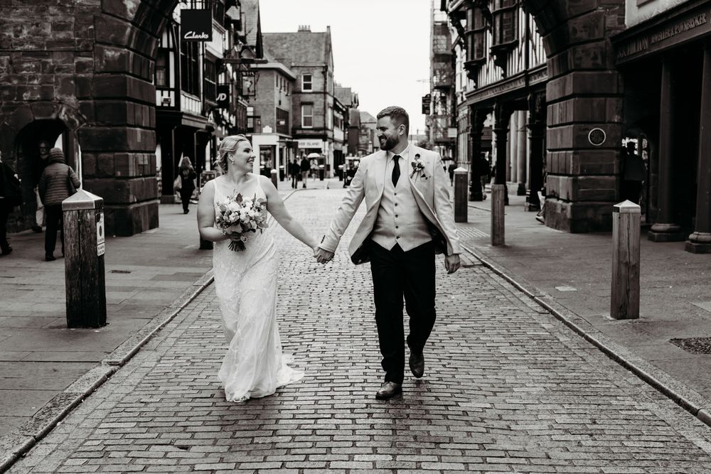 Black and white photo on cobblestone street with historic buildings backdrop.