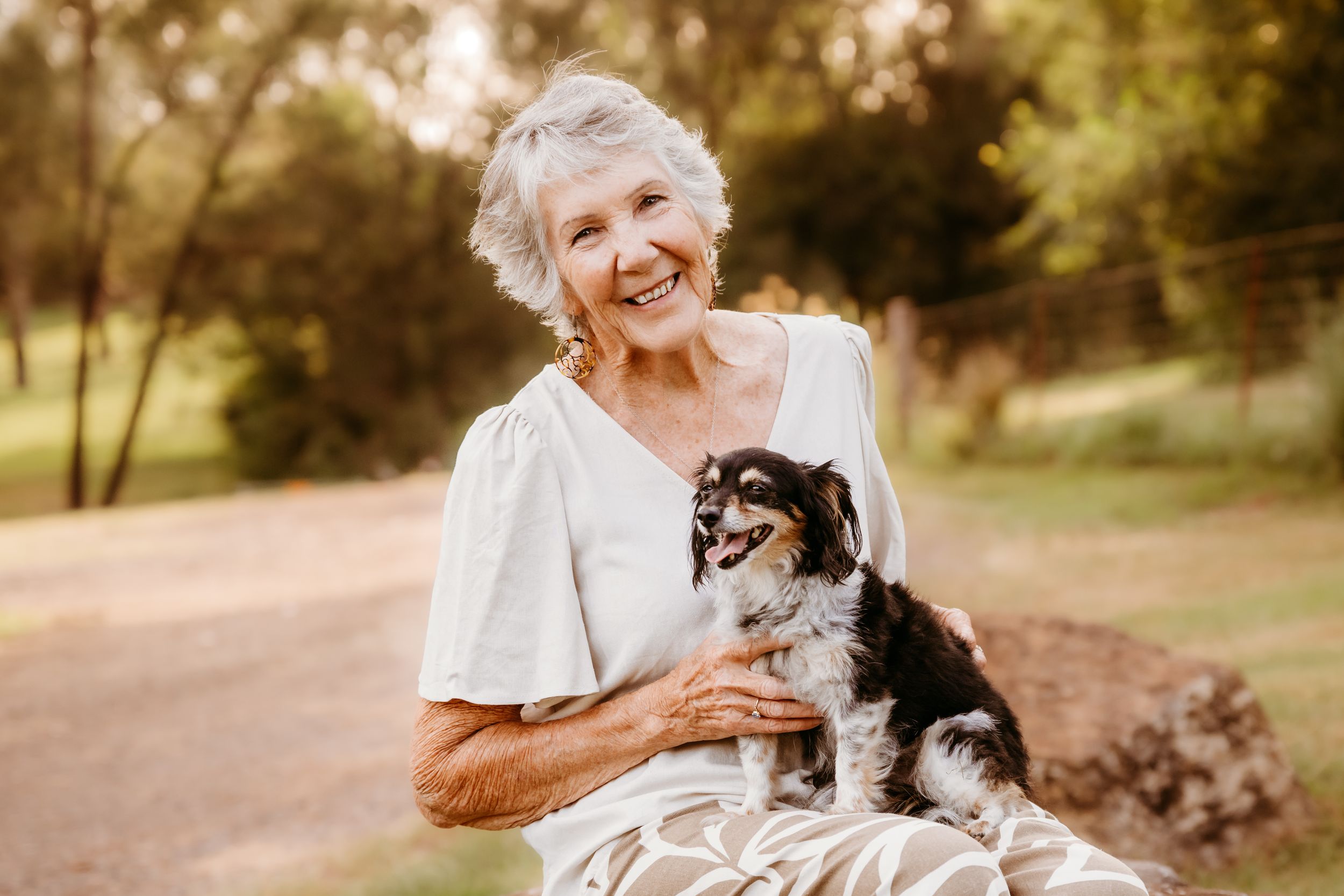 A person in white clothing holds and plays with a small black and brown dog outdoors during golden hour lighting.