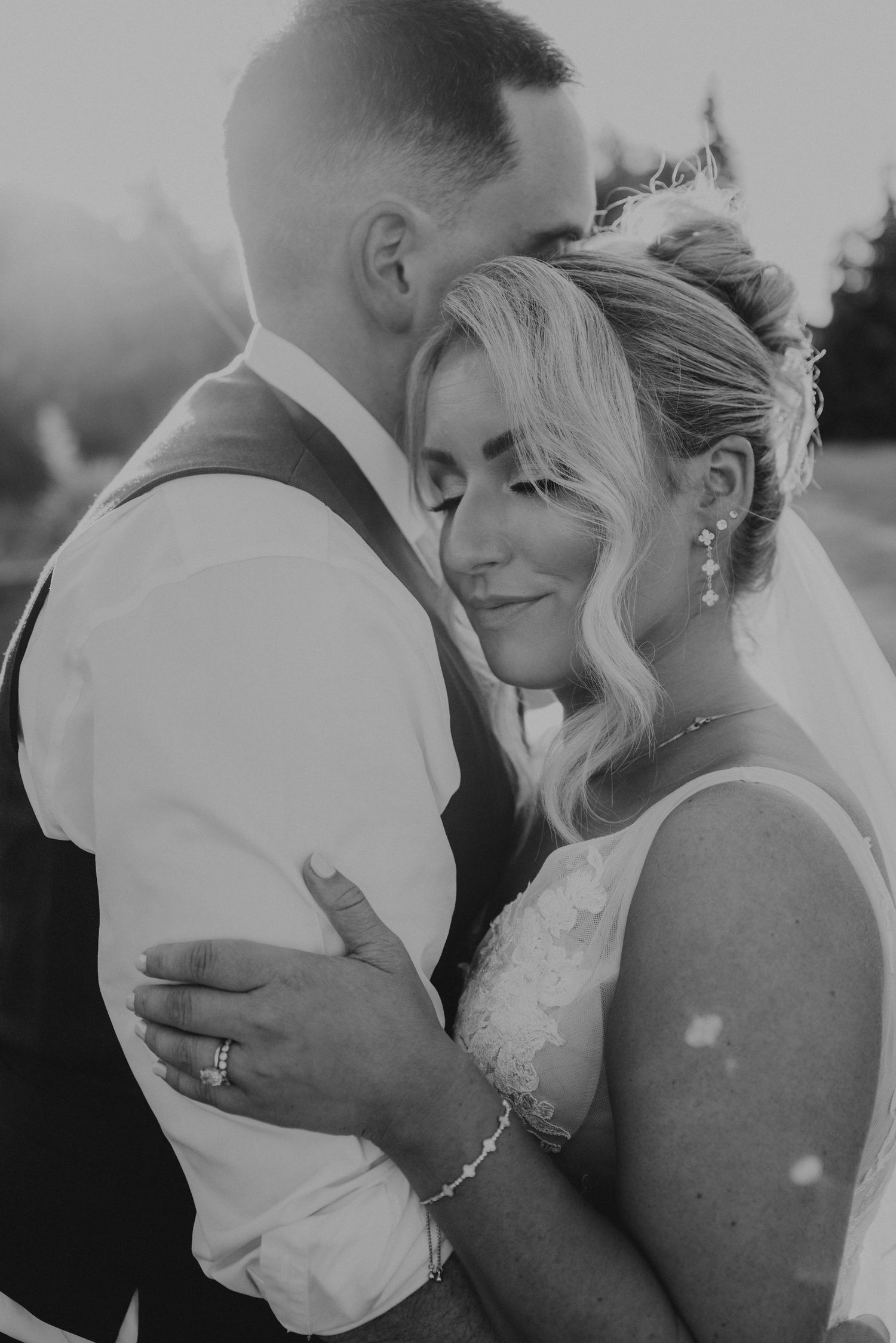 A tender wedding moment captured on a rooftop with the bride's veil flowing in the wind.