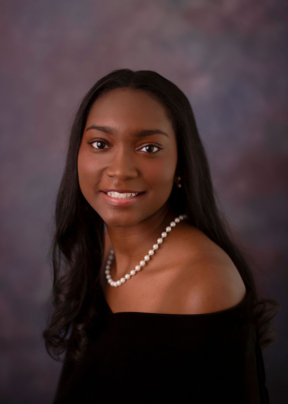Elegant portrait in black off-shoulder dress with pearl necklace against muted background.