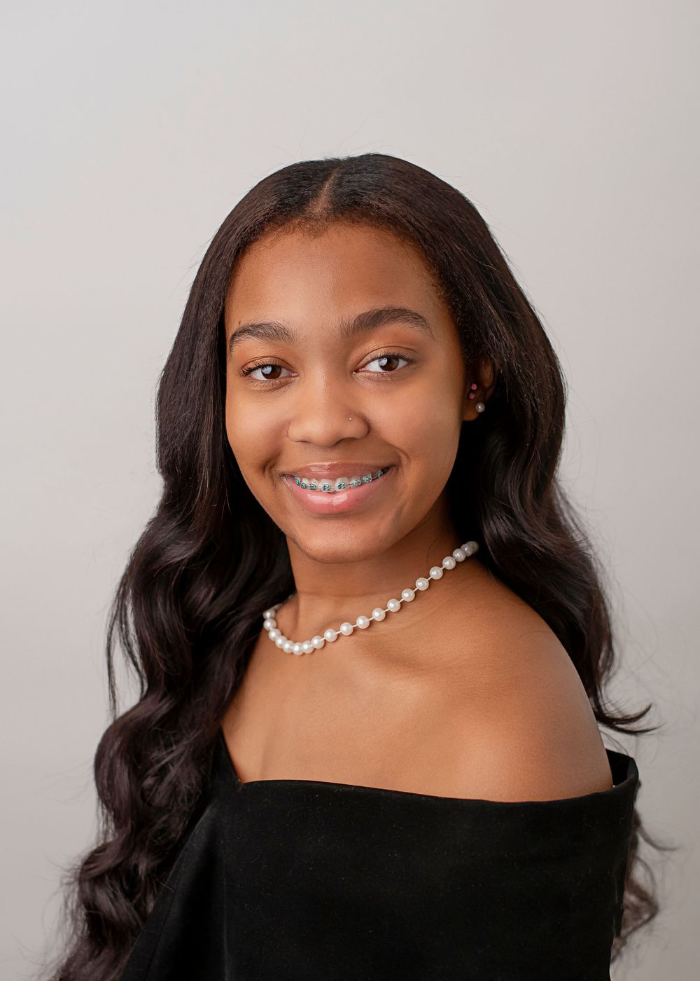 Professional studio portrait of someone in a black off-shoulder top with long wavy dark hair and a pearl necklace.