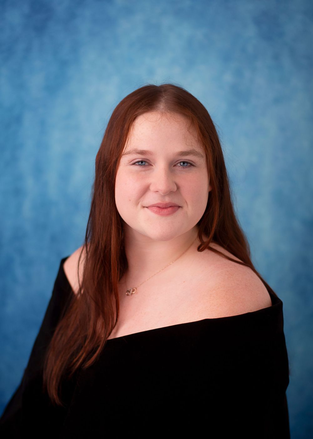 Portrait against blue backdrop wearing black off-shoulder top.