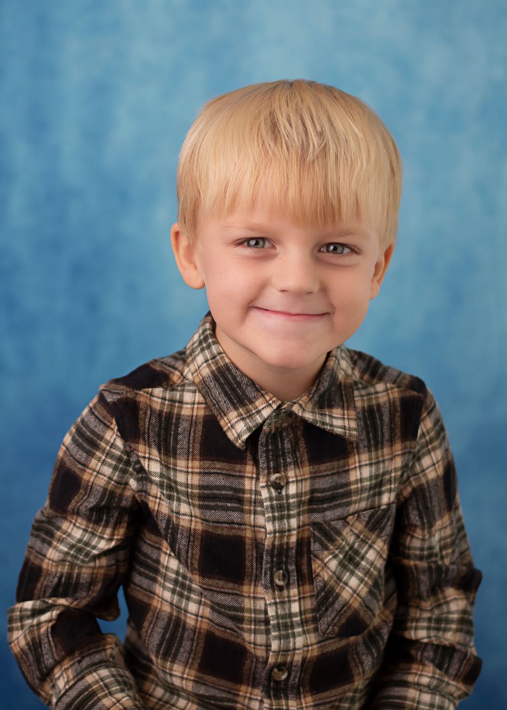 Studio portrait of a young child wearing a plaid flannel shirt against a blue backdrop.