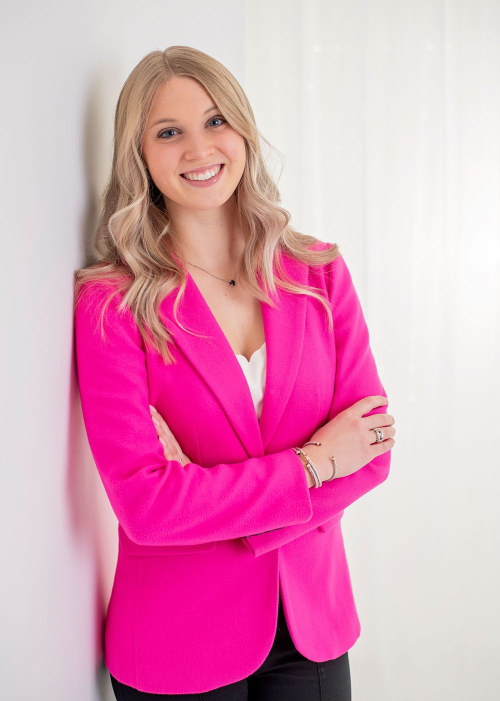 Professional portrait of someone wearing a vibrant hot pink blazer and white top against a light background.