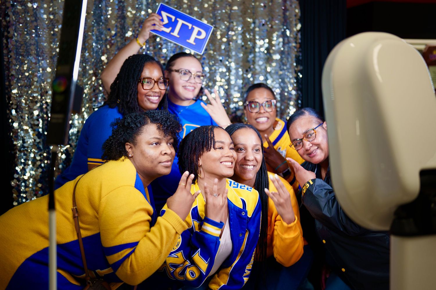 Group celebration photos with blue and yellow attire against sparkly backdrop.