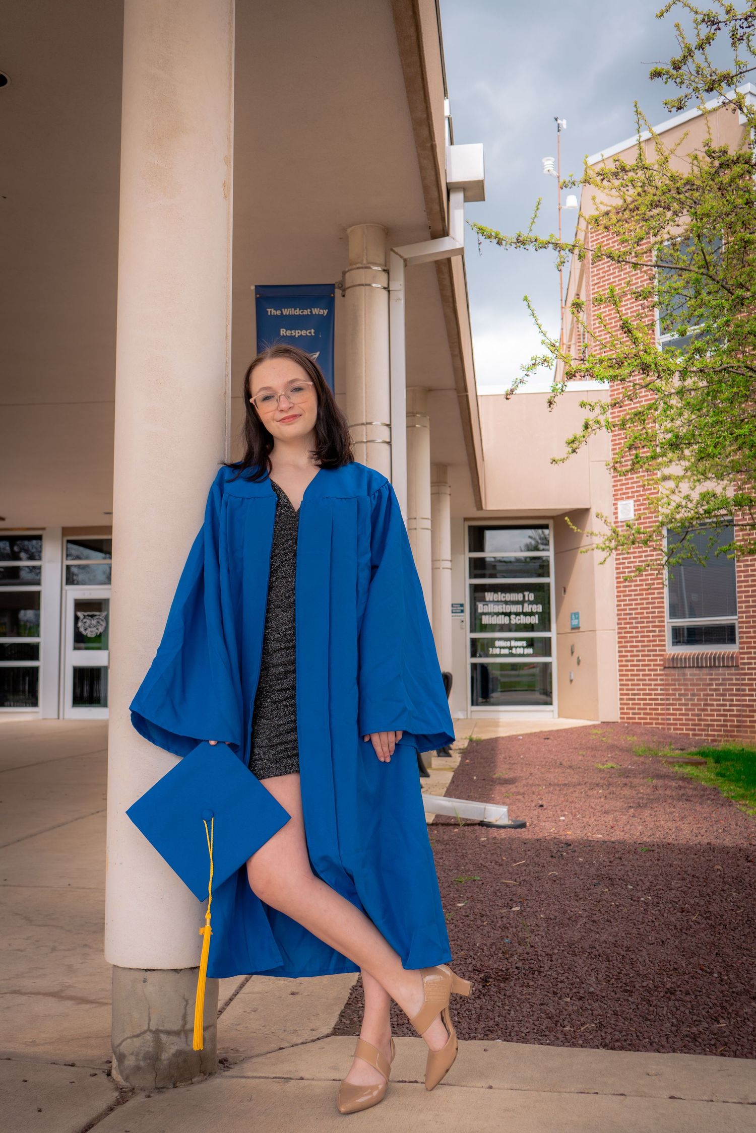 College graduate in blue graduation gown posing elegantly outside academic building.