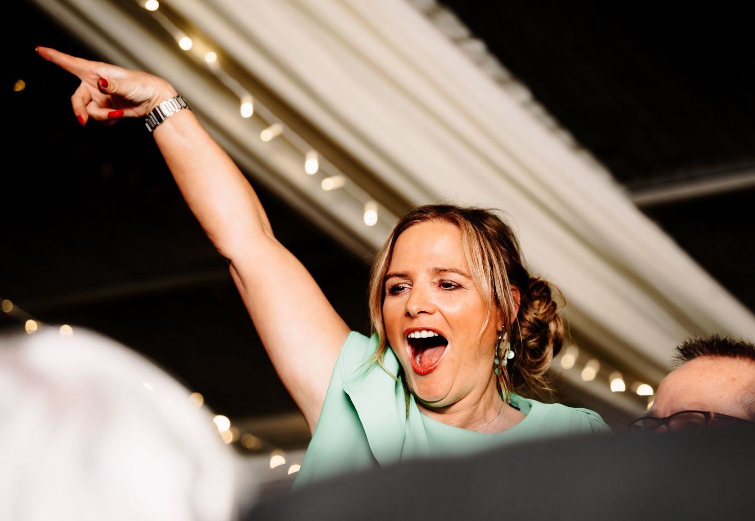 A joyful celebration moment captured with raised arms and bright lights in the background.