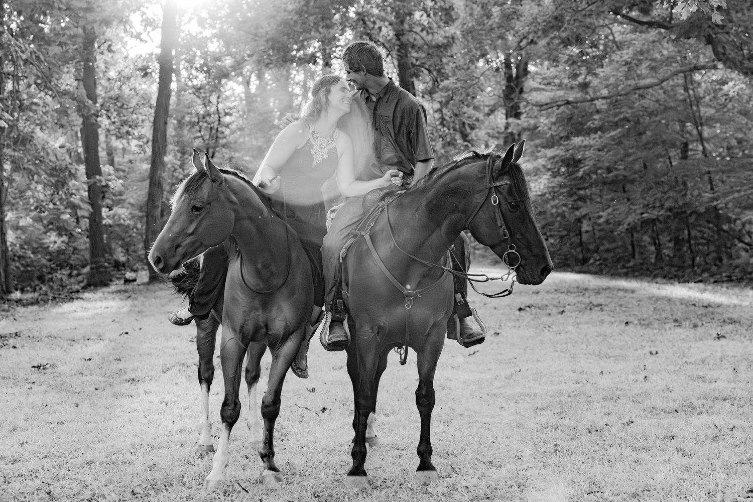 A black and white photo shows someone riding two horses simultaneously in a wooded area.