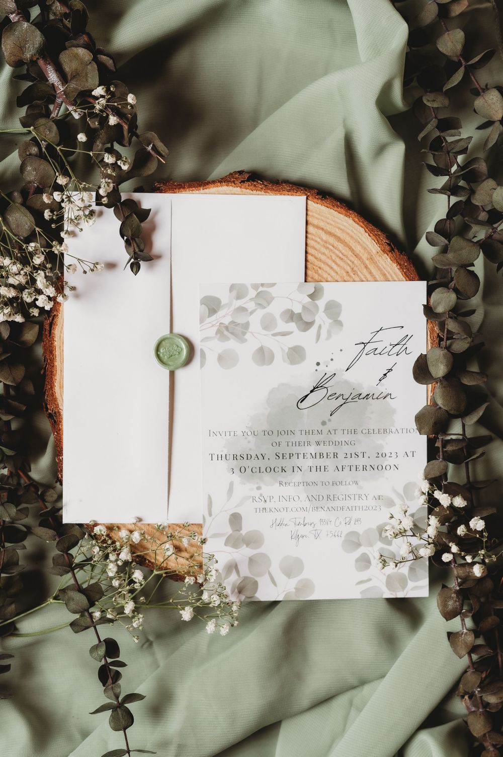 Elegant wedding invitation with leaf motifs displayed on wooden slice with eucalyptus and baby's breath.