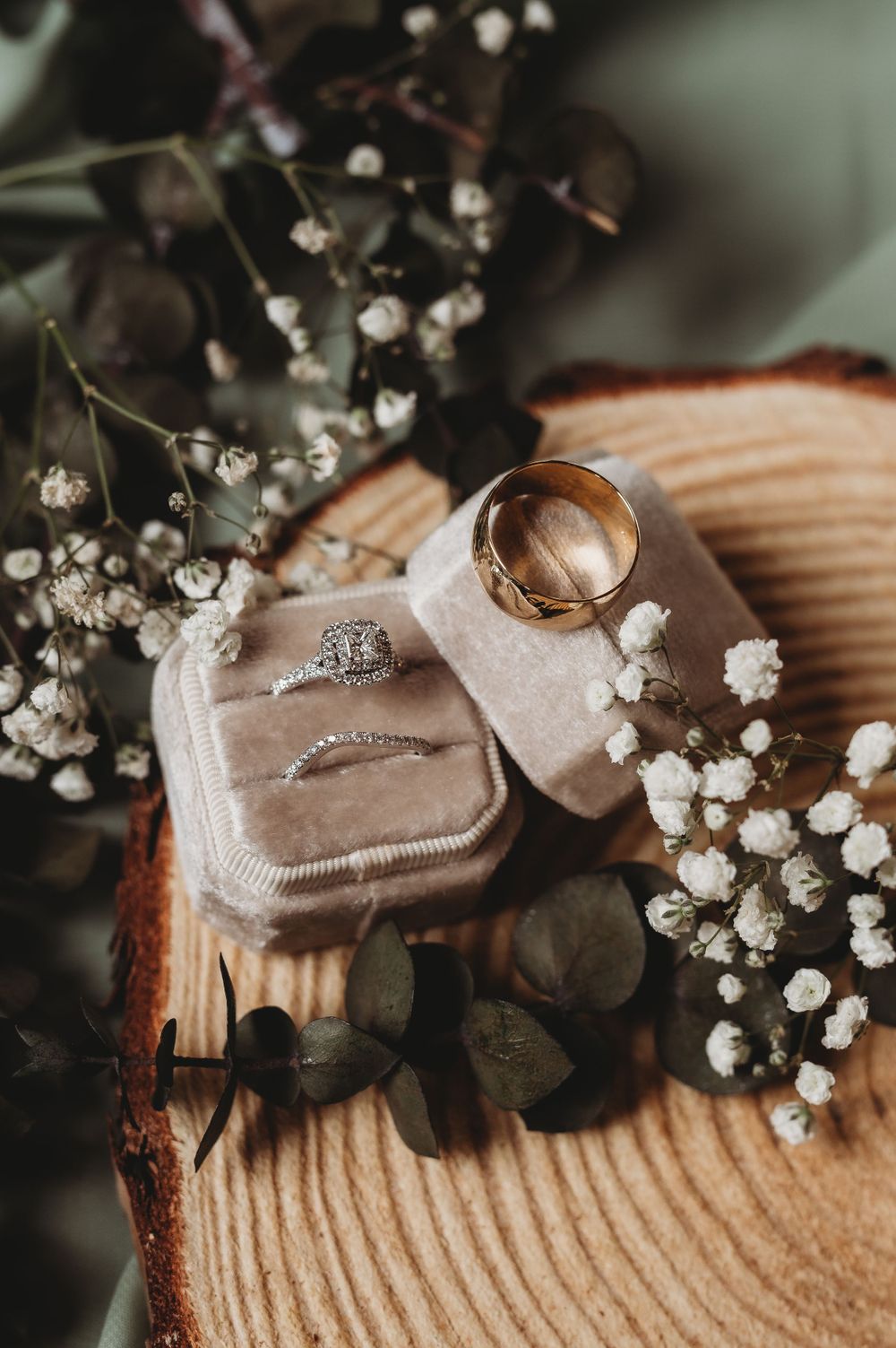 Wedding rings and engagement ring displayed in velvet box with delicate baby's breath flowers.