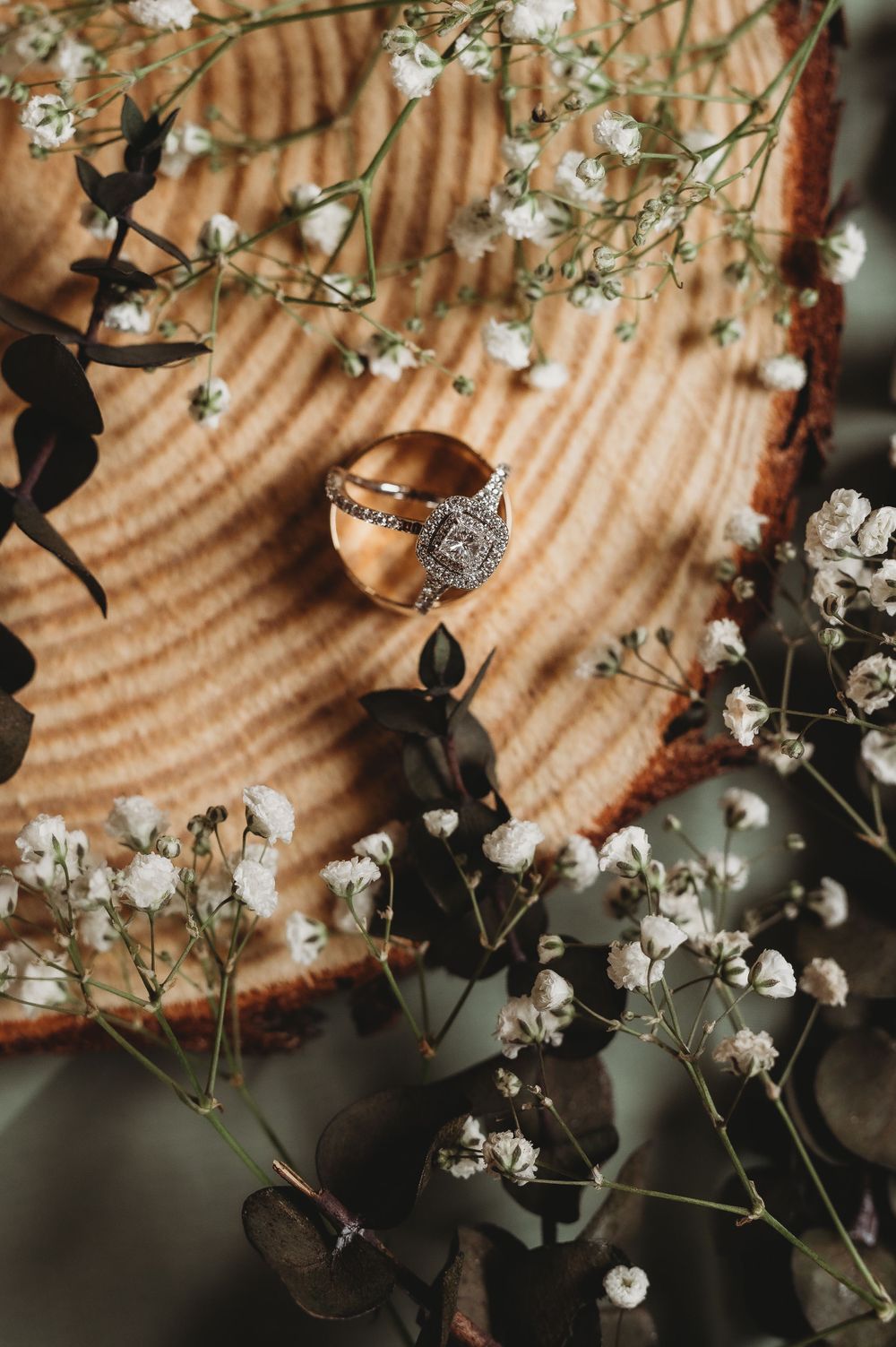 Rose gold wedding ring photographed on wooden surface with baby's breath flowers.