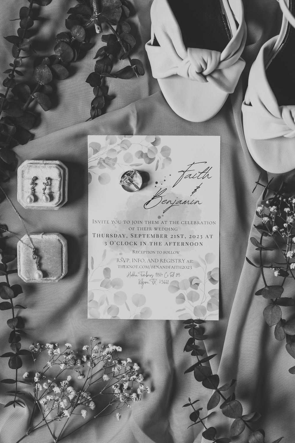Black and white wedding invitation styled with white flowers and eucalyptus on light fabric.