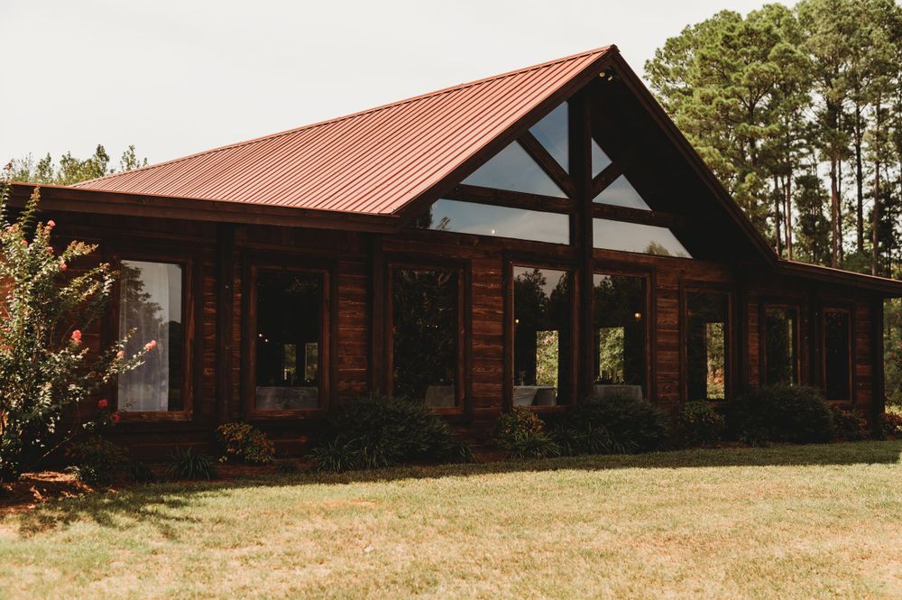 Rustic wooden venue with red metal roof and large windows in natural setting.