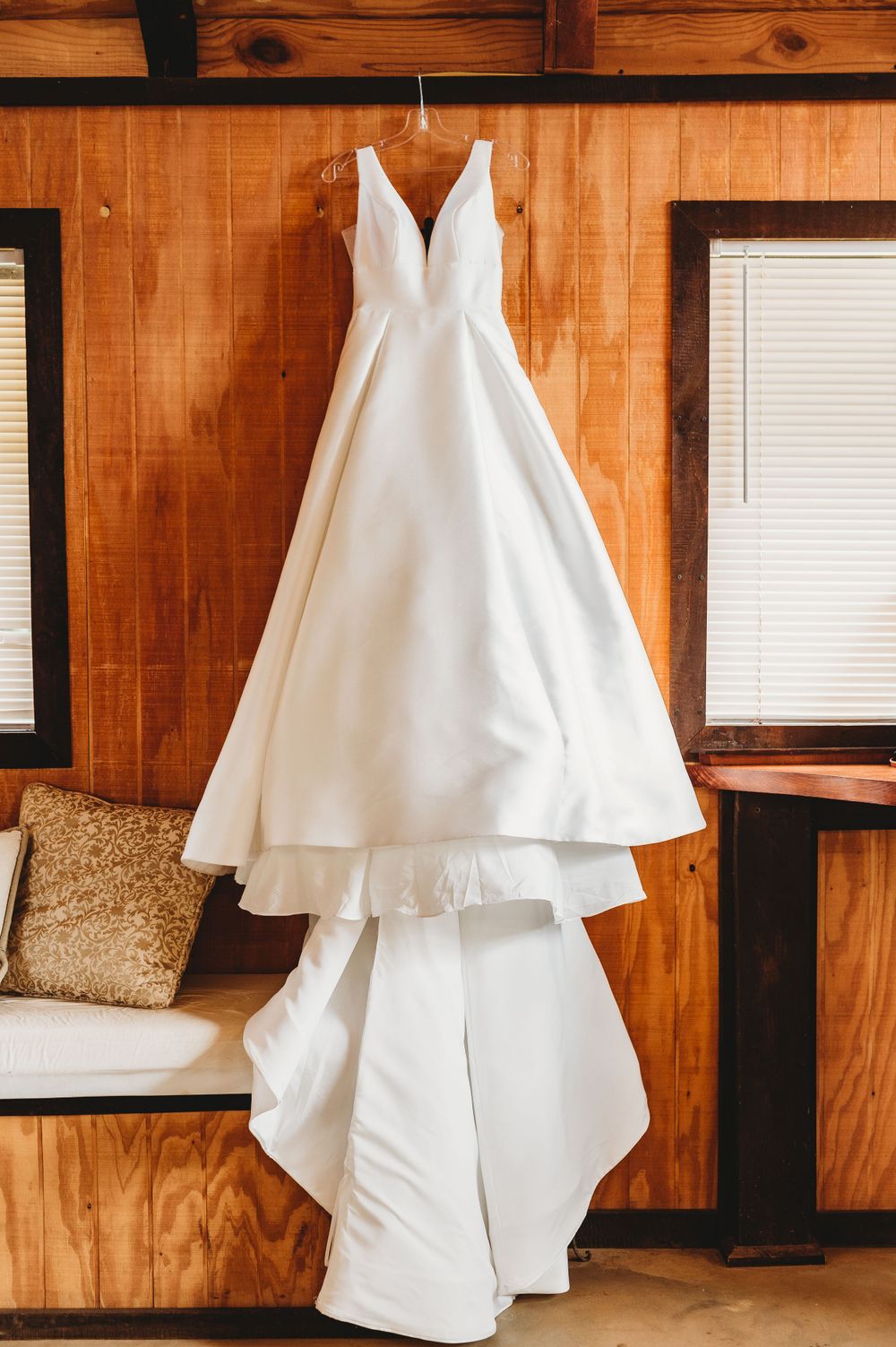 Elegant white wedding dress with v-neckline hanging on wooden paneled wall.