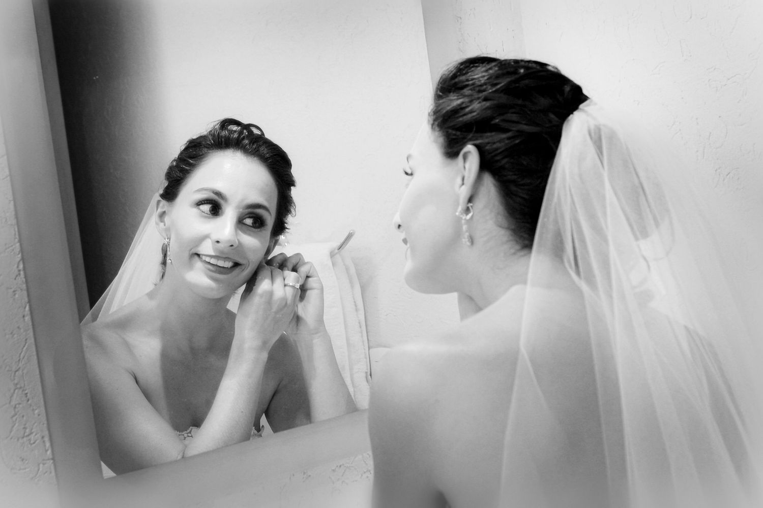 Artistic black and white photo of a bride looking in mirror while getting ready.