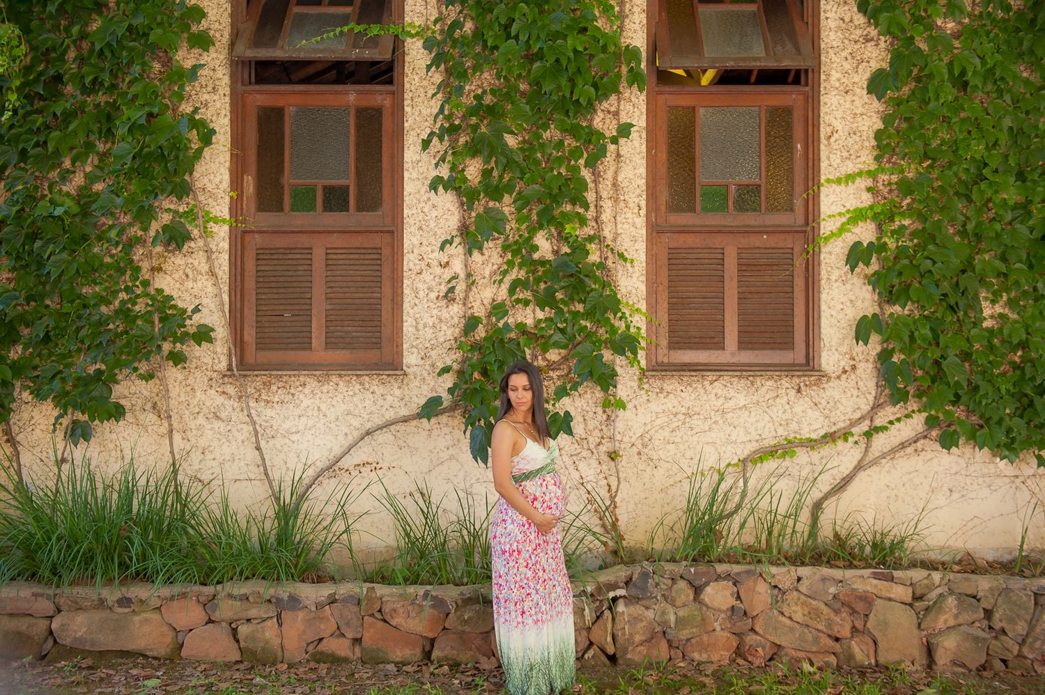A woman stands by a historic building with climbing vines framing two windows.