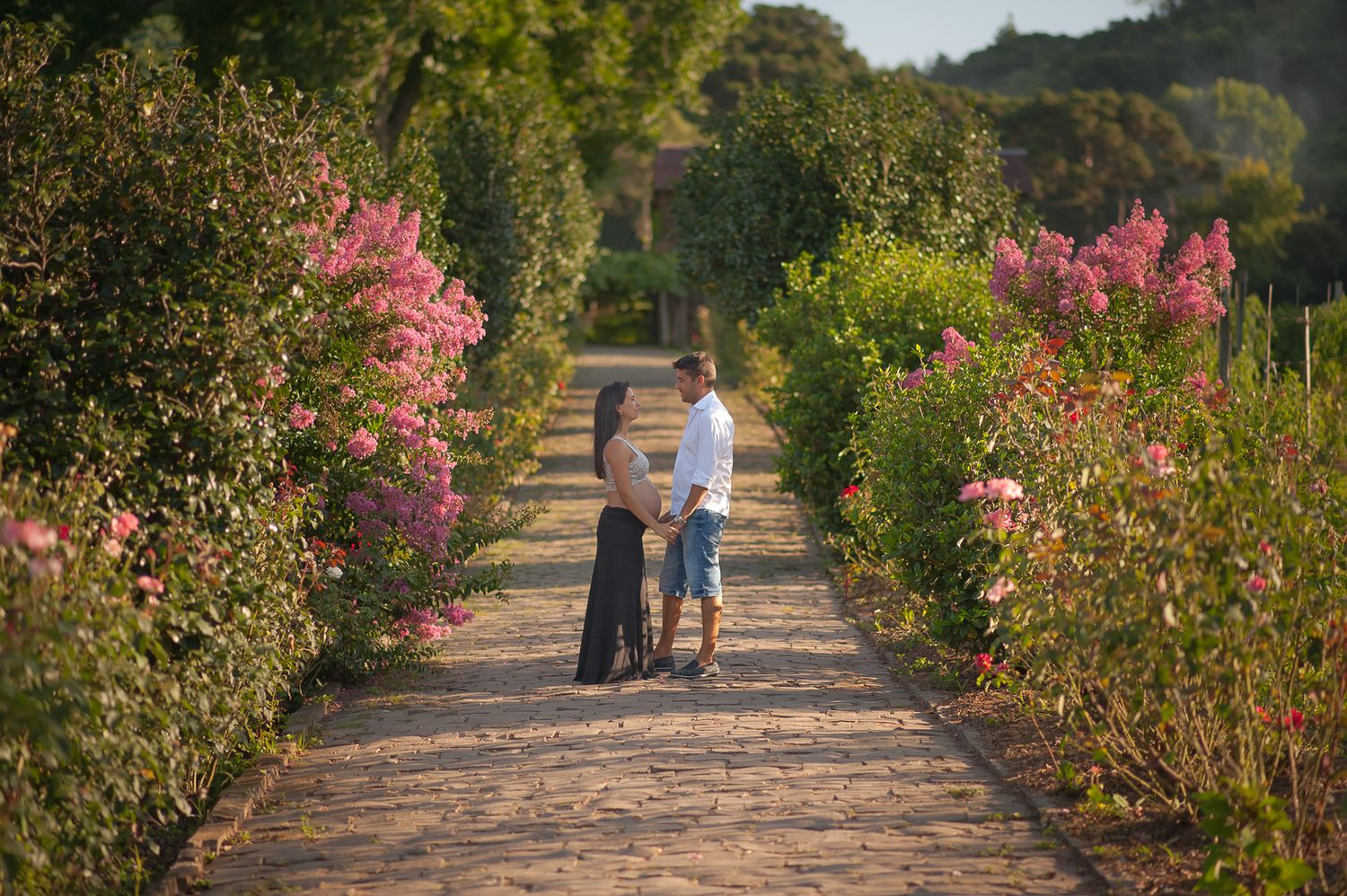 A pair walk down a garden path lined with blooming pink flowers.