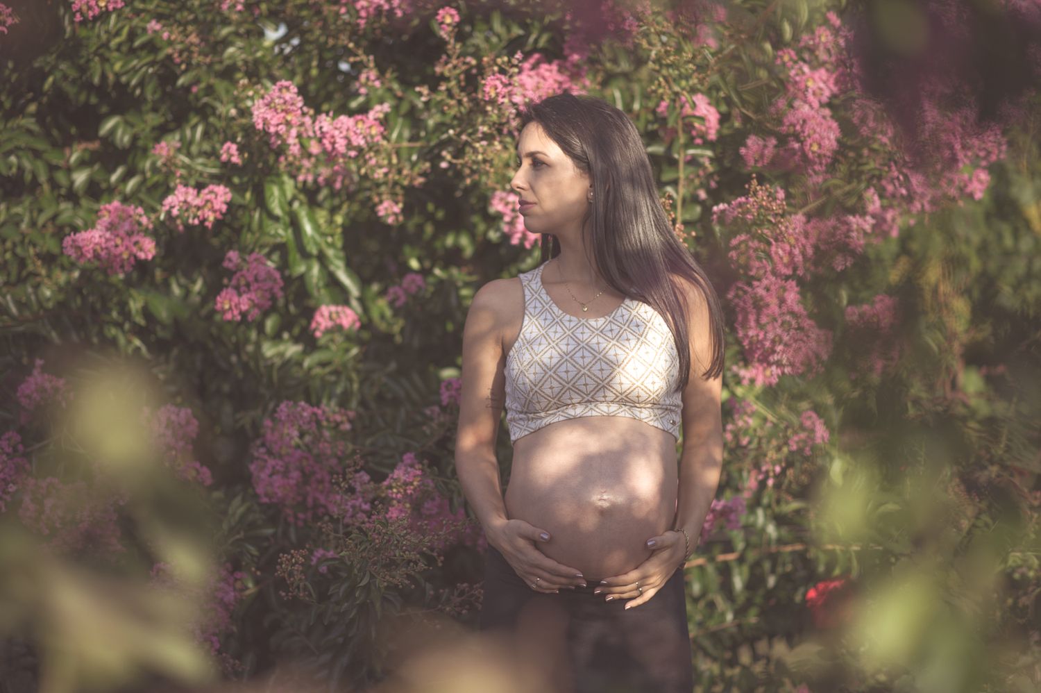 A maternity photo shoot among beautiful pink flowering bushes in soft sunlight.