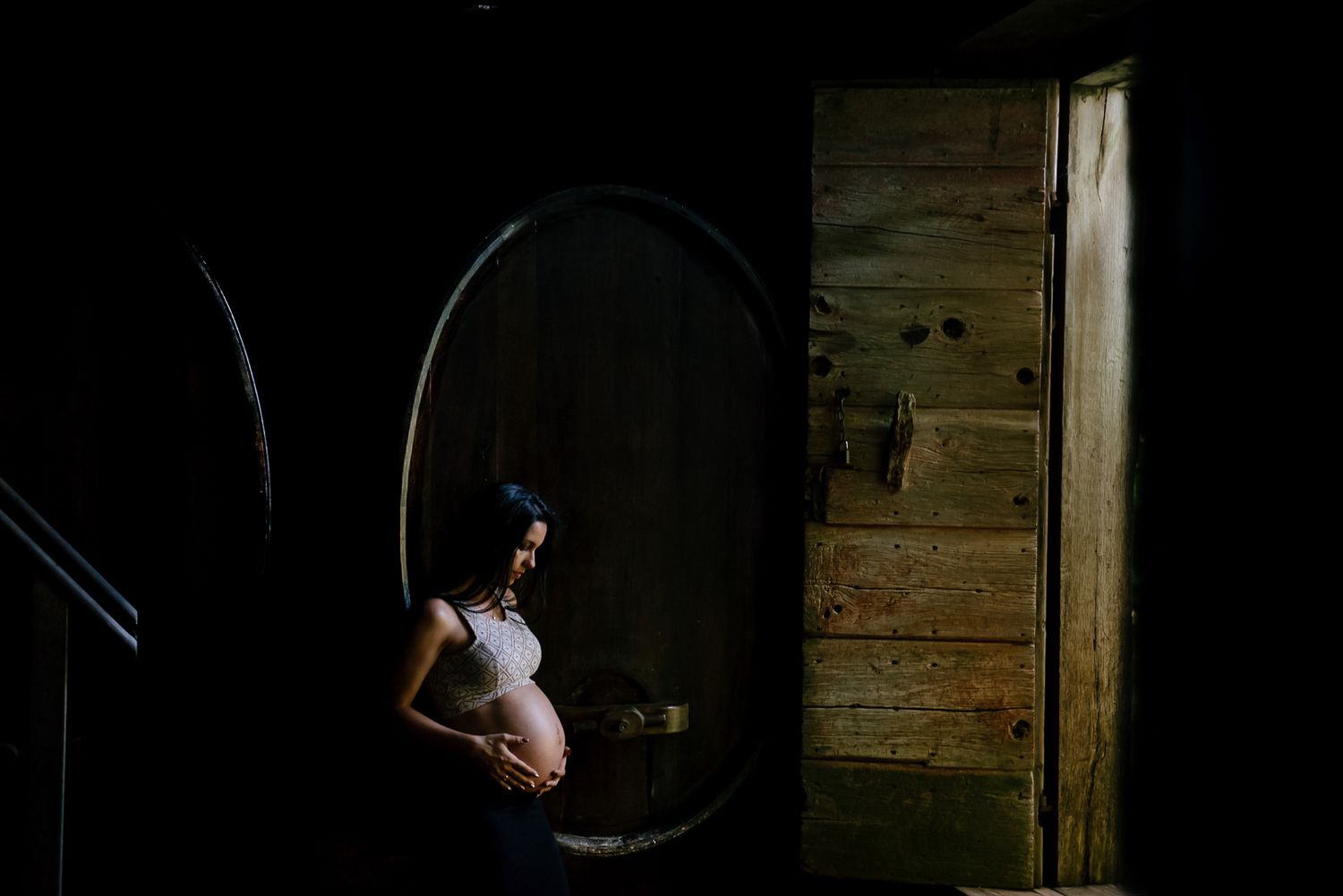 A dramatic maternity silhouette posed in a rustic wooden doorway.